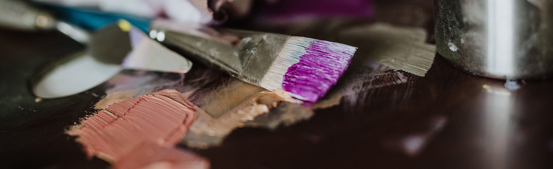 A brush covered in pink paint laying on the palette